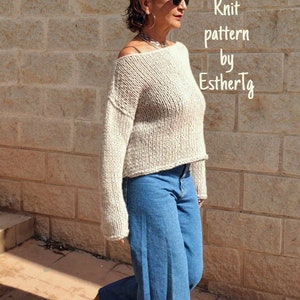 May include: A woman wearing a beige knitted sweater with a loose fit and long sleeves. She is wearing blue jeans and brown shoes. The text "Sweater Knit pattern by EstherTg" is visible in the image.