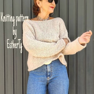 May include: A knitted sweater in a light beige color with a loose fit and long sleeves. The sweater has a slightly dropped shoulder and a wide neckline. The model is wearing the sweater with blue jeans.