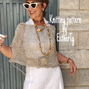 May include: A woman wearing a white top, a beige crochet poncho, a white skirt, and beige heels. She is standing in front of a brick wall and a wooden door. The text "Knitting pattern by EsthertG" is written on the wall.
