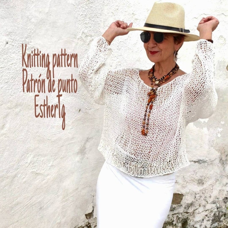 Pu&ograve; includere: Top bianco in crochet con una vestibilit&agrave; ampia e maniche lunghe. Il top &egrave; indossato da una persona con un cappello bianco e una lunga collana con perline marroni.
