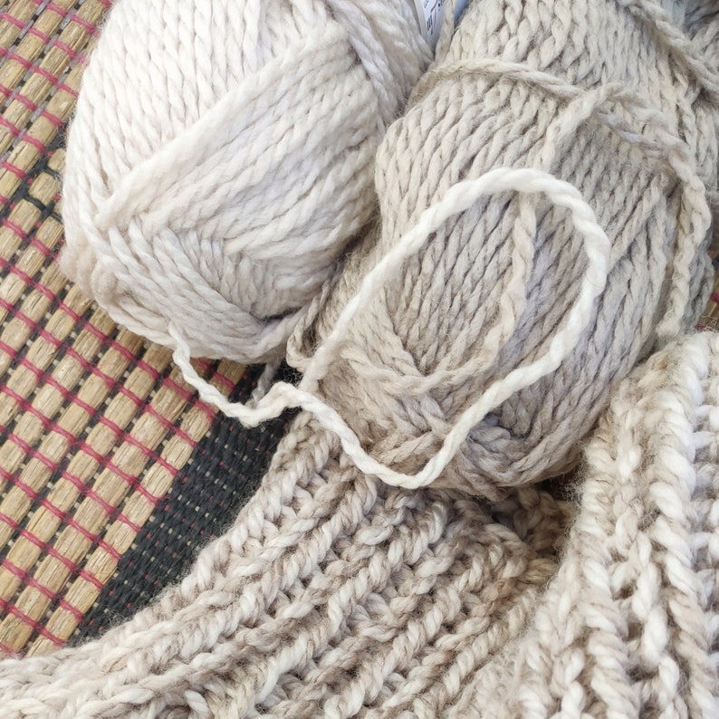 May include: Two balls of beige yarn with a white yarn tied around them. The yarn is soft and fluffy and would be great for knitting or crocheting.