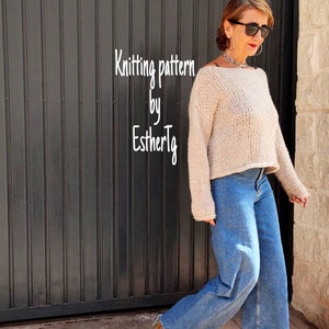May include: A woman wearing a beige knitted sweater with a wide neckline and long sleeves. She is wearing blue jeans and brown heeled boots. The sweater is a knitted pattern by EstherTlg.