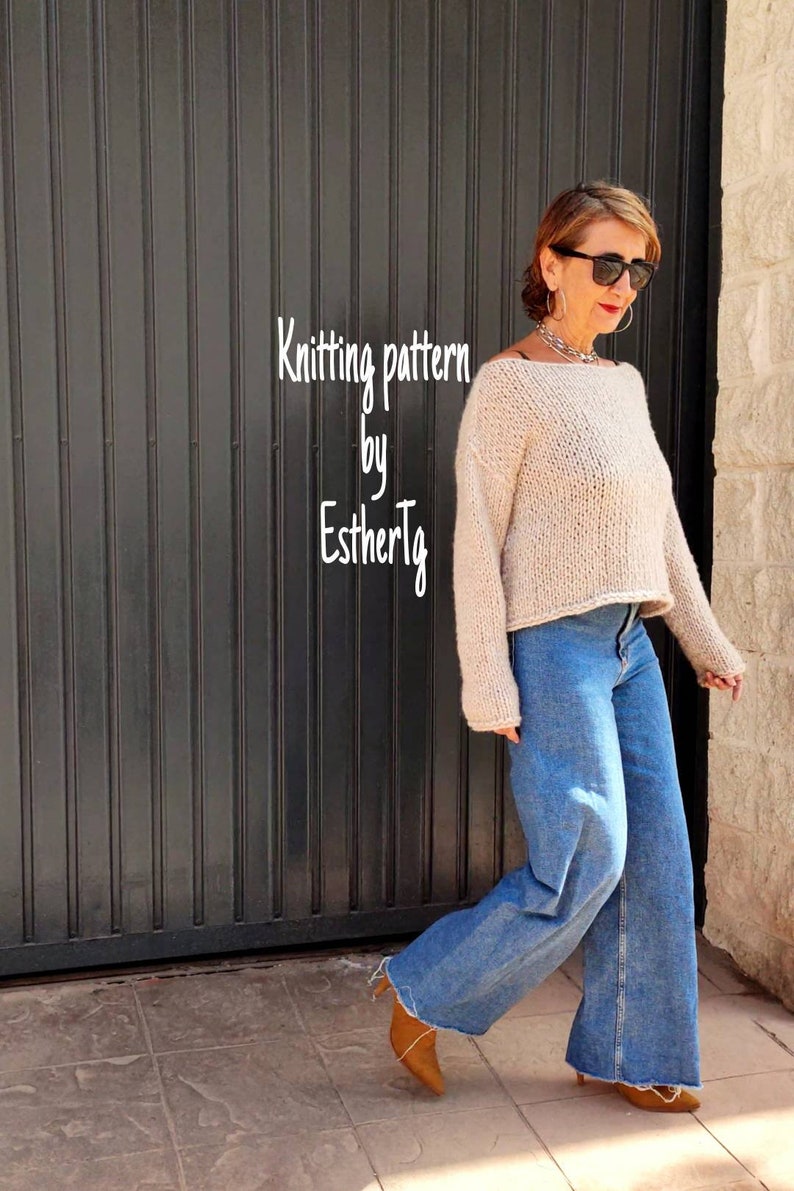 May include: A woman wearing a beige knitted sweater with a wide neckline and long sleeves. She is wearing blue jeans and brown heeled boots. The sweater is a knitted pattern by EstherTlg.