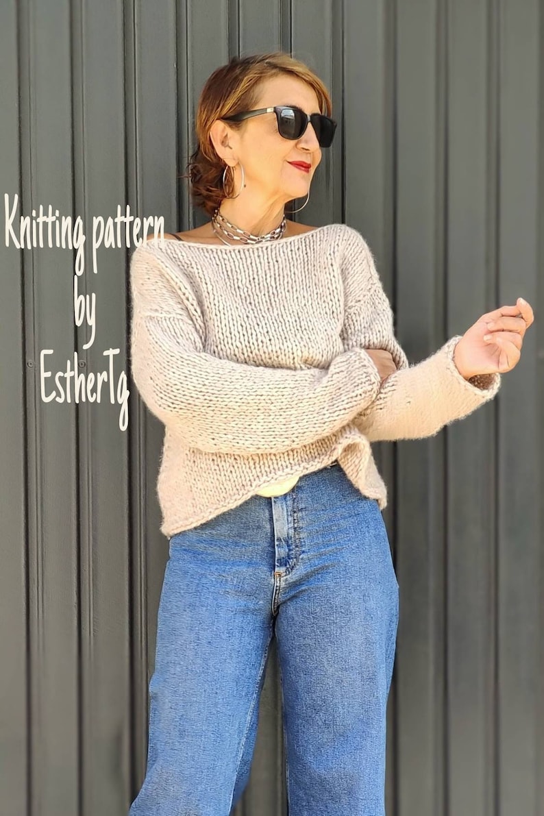 May include: A knitted sweater in a light beige color with a loose fit and long sleeves. The sweater has a slightly dropped shoulder and a wide neckline. The model is wearing the sweater with blue jeans.
