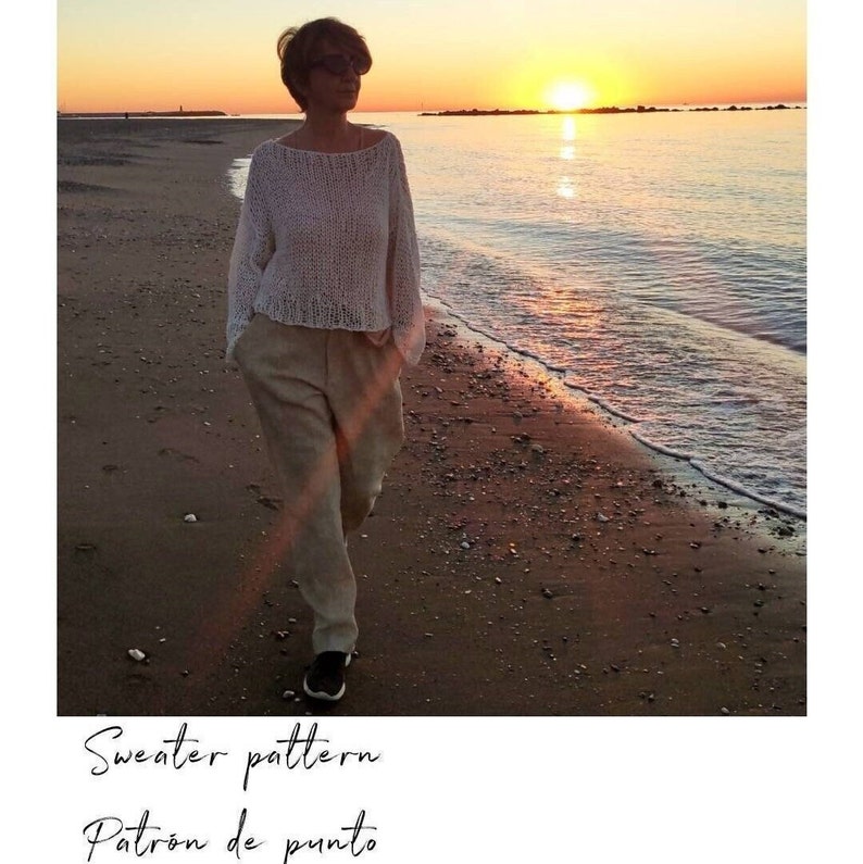 Pu&ograve; includere: Una donna cammina lungo una spiaggia sabbiosa al tramonto indossando un maglione bianco lavorato a maglia e pantaloni beige. Il testo "Sweater pattern Patron de punto" &egrave; in basso nell'immagine.