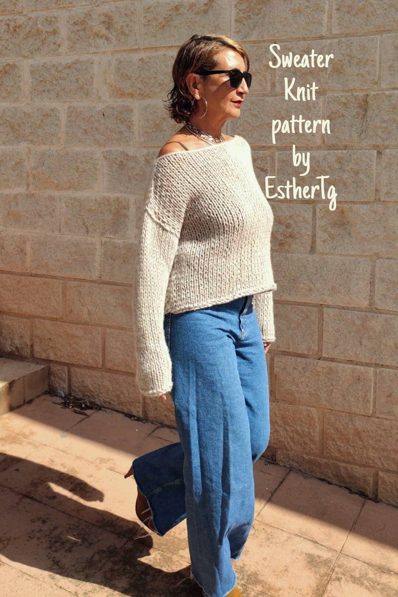 May include: A woman wearing a beige knitted sweater with a loose fit and long sleeves. She is wearing blue jeans and brown shoes. The text "Sweater Knit pattern by EstherTg" is visible in the image.