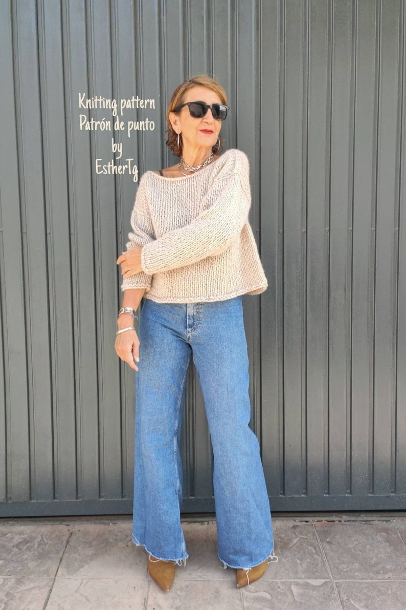 May include: A woman wearing a beige knitted sweater with a loose fit and long sleeves. She is also wearing blue jeans and brown heeled shoes. The sweater has a simple design and is a great choice for casual wear.