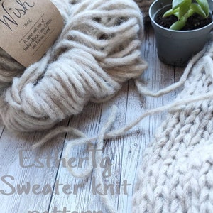 May include: A close-up of a ball of beige yarn with a brown label that reads "A super soft mix of Baby Alpaca, Pima Cotton and Merino Wool". The yarn is next to a knitted sweater made with the same yarn. The text "Estherty Sweater Knit Pattern" is written on the wooden surface.