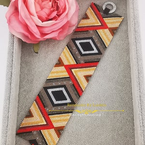 May include: A beaded bracelet featuring a geometric pattern in shades of brown, red, gold, and black. The bracelet has a silver clasp and is displayed in a grey velvet box. "Renovatio By Lucia" and "All Rights Reserved" are printed on the bracelet.