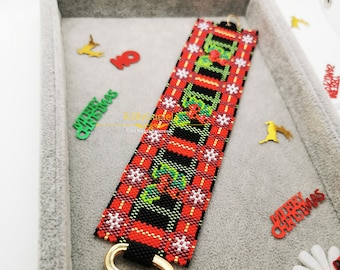 May include: A red, green, and black beaded bracelet with a gold charm in the shape of a bell with a red bow. The charm is attached to the bracelet with a gold loop. The bracelet is in a gray velvet box with gold trim.