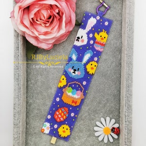 Può includere: Un braccialetto di perline viola con un tema pasquale colorato. Il braccialetto presenta un coniglietto, pulcini, uova e un cestino. Il braccialetto è in una scatola di velluto grigio con una rosa rosa e una margherita bianca.