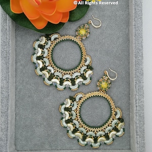 Op de afbeelding: Een paar handgemaakte kralen oorbellen met een cirkelvormig ontwerp. De oorbellen hebben een goudkleurig kralenframe, een donkergroene binnenste cirkel van kralen en witte en lichtgroene accenten. De oorbellen hebben een gele edelsteen aan de bovenkant.