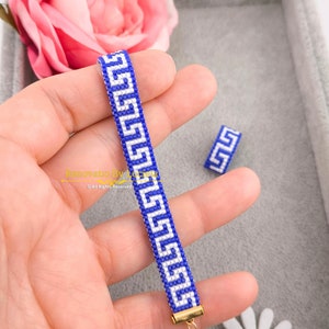 May include: A blue and white beaded bracelet with a Greek key pattern. The bracelet is made with small beads and has a gold clasp.
