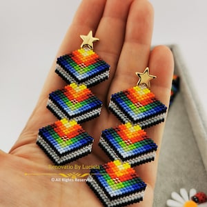 May include: A pair of long, colorful beaded earrings with a star charm at the top. The earrings are made of small, colorful beads in a geometric pattern. The earrings are hanging from a person's hand.