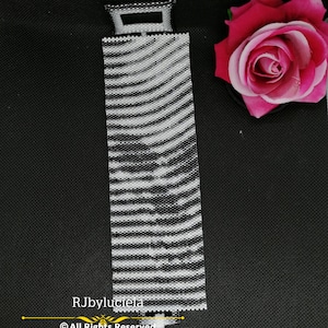 Può includere: Un aereo di perline bianco e nero con una pista di atterraggio a strisce bianco e nero. La pista è fatta di perline e ha un piccolo finestrino di perline in cima. L'aereo è su una superficie nera. Il testo "RJbyluciela © All Rights Reserved" è sotto la pista.