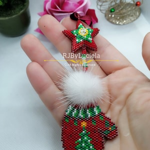 May include: Red and green beaded Christmas ornament shaped like a mitten with a white pom-pom on top. The mitten has a small green beaded Christmas tree on the front. A red beaded star with a green center and a white rhinestone is attached to the top of the mitten.