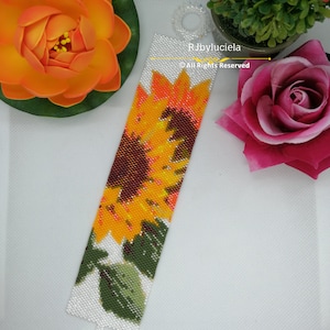 May include: A white beaded bracelet with a colorful sunflower design. The bracelet has a clasp and is made with small beads. The text "RJbyluciela &copy; All Rights Reserved" is printed on the bracelet.