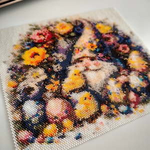 Peut inclure: Gros plan sur une œuvre d'art en perles représentant une couronne de fleurs jaunes, orange, roses et violettes entourant un oiseau blanc avec des poussins jaunes. Les perles sont disposées en mosaïque, créant une image détaillée et colorée.