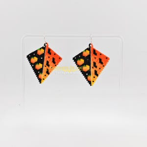 Peut inclure: Une paire de boucles d'oreilles faites à la main, perlées. Chaque boucle d'oreille est en forme de losange, divisée en diagonale. Une moitié est noire avec des détails de citrouille orange, l'autre moitié est orange avec des taches noires.
