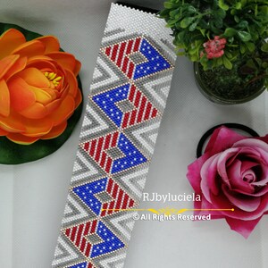 May include: A white beaded bracelet with a repeating pattern of American flags in red, white, and blue. The bracelet is made with small beads and has a chevron pattern.