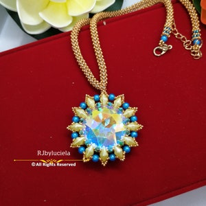 May include: A gold-toned necklace with a large, iridescent pendant. The pendant is surrounded by light blue and cream-colored beads. The necklace is displayed on a red surface. The text "RJbyluciela" and "© All Rights Reserved" are visible.