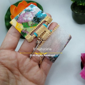 May include: A pair of colourful beaded earrings with a gold-tone metal clasp. The earrings are made with small beads in a variety of colours, including pink, blue, green, and yellow. The earrings are hanging from a gold-tone metal chain.