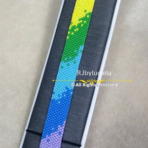 Pode incluir: Um bracelete de contas de arco-íris com um fecho de corrente de prata. O bracelete está em um expositor preto. RJbyluciela © Todos os direitos reservados.