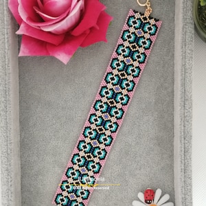 May include: A pink and blue beaded bracelet with a geometric pattern. The bracelet has a gold clasp and is made with small, colourful beads.