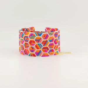 May include: A colourful beaded bracelet with a geometric pattern in shades of orange, pink, blue, and white. The bracelet is made with small, evenly spaced beads and has a clasp closure.