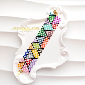 May include: A colorful beaded bracelet with a geometric pattern of triangles in various colors, including pink, green, blue, and yellow. The bracelet has a gold-colored clasp and is displayed on a white, decorative plate. The text "Renovatio By Luciela" is visible.
