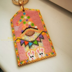 May include: A pink and gold beaded keychain with a gnome wearing a colorful hat and holding a string of flags. Two white beaded bunnies are at the bottom of the keychain.