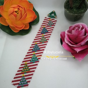 May include: A red, white and green beaded bracelet with a Christmas tree design. The bracelet is made with small beads and has a clasp closure. The bracelet is on a white background.