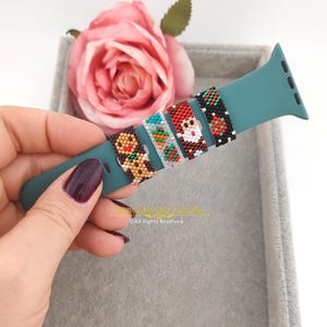 Può includere: Cinque bande colorate con perline per un Apple Watch. Le bande presentano vari disegni a tema natalizio, tra cui un omino di pan di zenzero, un pupazzo di neve, Babbo Natale e una renna. Le bande sono mostrate su un cinturino Apple Watch verde acqua.