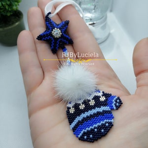 May include: A blue and white beaded ornament shaped like a mitten with a white fur pom-pom on top. A blue beaded star with a silver rhinestone in the centre hangs above the mitten.