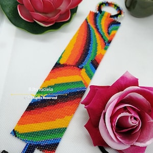 May include: A colourful beaded bracelet with a rainbow pattern. The bracelet is made with small, colourful beads and has a black clasp. The bracelet is lying on a white surface.