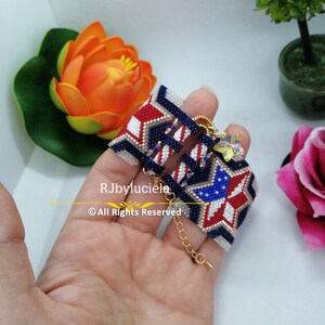 May include: A beaded bracelet with a star design in red, white, and blue colors. The bracelet has a gold chain clasp and a small charm.