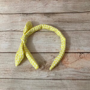 May include: A yellow and white checkered headband with a bow on the side.