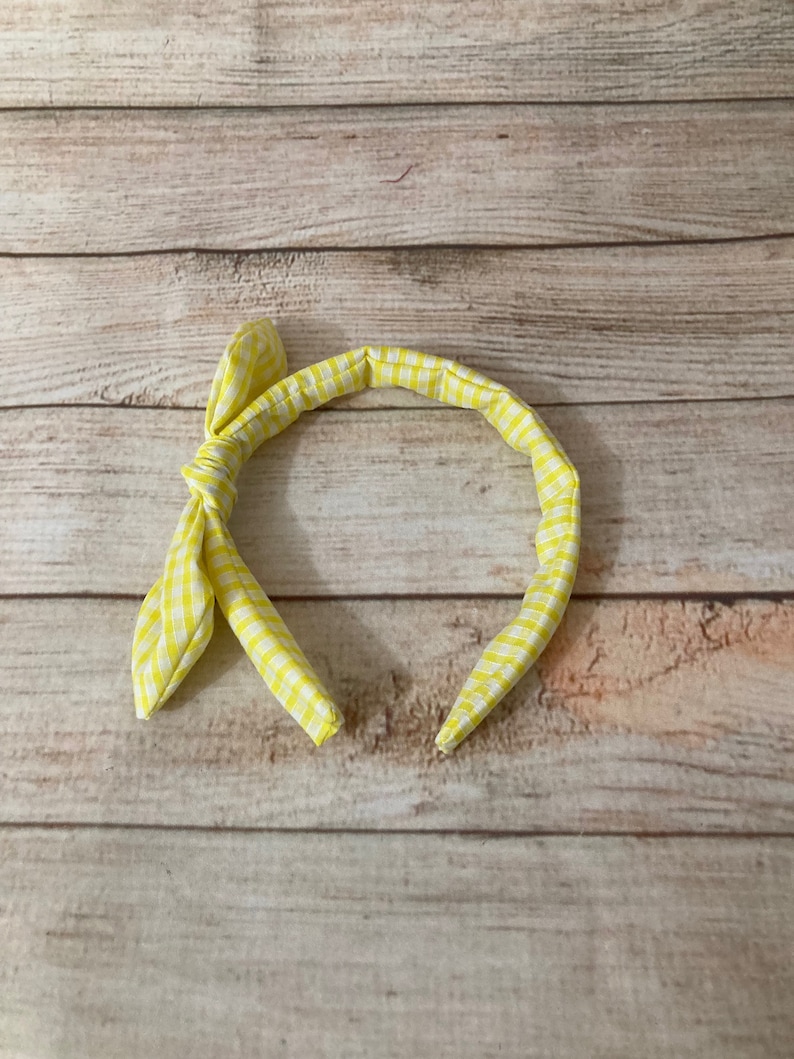 May include: A yellow and white checkered headband with a bow on the side.