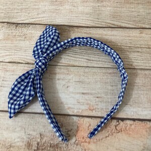 May include: A blue and white gingham headband with a bow on the side.