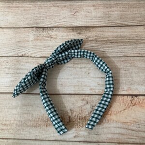 May include: A green and white gingham headband with a bow on the top.