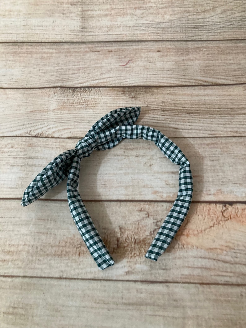 May include: A green and white gingham headband with a bow on the top.