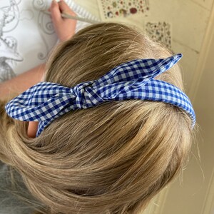 May include: A blue and white gingham headband tied in a knot on top of the head.