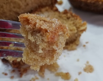 May include: Close-up of a piece of golden-brown cake on a fork, with a sugar-coated top. The cake has a soft, textured appearance, with visible crumbs. Other pieces of cake are in the background, suggesting a baked treat.