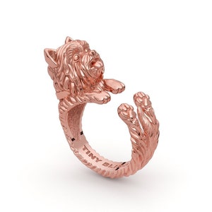 May include: Rose gold ring featuring a detailed sculpture of a Yorkshire Terrier dog. The dog is depicted in a playful pose with its paws raised. The ring is inscribed with the words "Tiny Bliss".