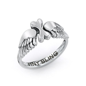 May include: Silver ring with two angel wings on the band. The band is engraved with the words "TINY BLING".