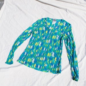 May include: A blue, green, and white floral long-sleeved shirt with a V-neck. The shirt has a label that reads "VERSACE COLLECTION" and "1".