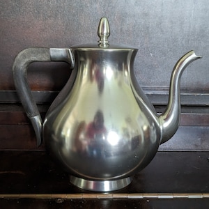 May include: A silver teapot with a rounded body and a curved spout. The teapot has a wooden handle and a shiny, reflective surface.