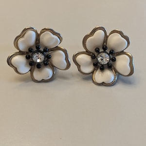 May include: A pair of white flower-shaped earrings with black accents and a clear rhinestone in the center.
