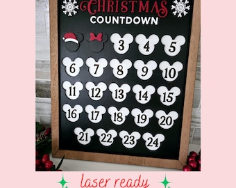 May include: A black chalkboard with a wooden frame features a Christmas countdown with Mickey Mouse ears. The chalkboard has the text "Christmas Countdown" and numbers 3 through 24 in white Mickey Mouse ears. The numbers are arranged in a grid of five columns and five rows. The top two Mickey Mouse ears have a red Santa hat and a red bow.