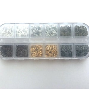 May include: A clear plastic organiser filled with small metal jump rings in various colours, including silver, gold, and black. The jump rings are neatly arranged in separate compartments, ideal for jewellery making and crafting projects.